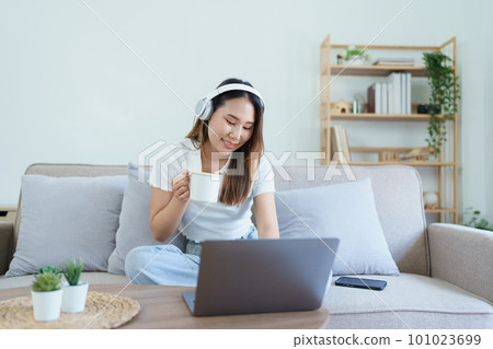 asian teenage girl using computer and wearing headphones at sofa. 101023699