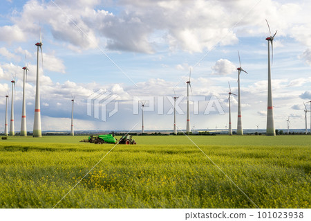 Scenic landscape view big modern tractor machine with sprayer equipment spraying fertilizer in rapeseed agricultural field against windfarm power windmill. Arable land cultivation sustainable energy 101023938