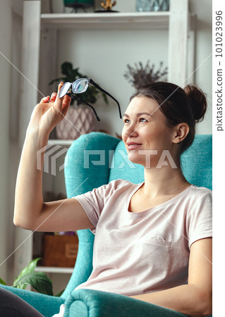 Young woman with glasses in hands sits in a chair Young woman with glasses in hands sits in a chair 101023996
