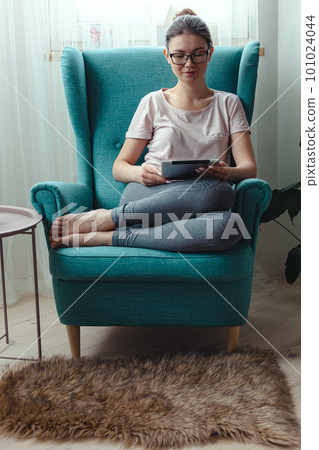Young woman using tablet while sitting in a comfortable chair 101024044