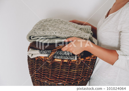 Stack of knitted sweaters on wicker basket in young female hands 101024064
