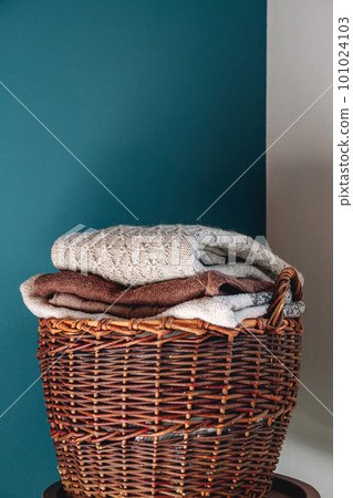 Stack of knitted sweaters on wicker basket. 101024103