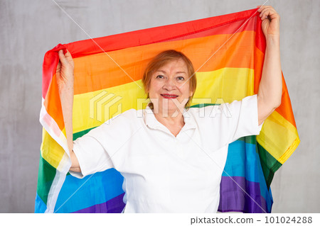 Cheerful senior woman standing confidently with rainbow flag 101024288