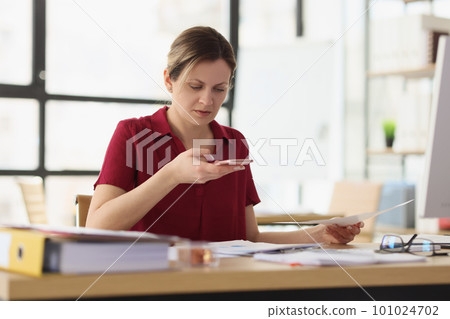 Woman with paper dials number on mobile phone in office 101024702