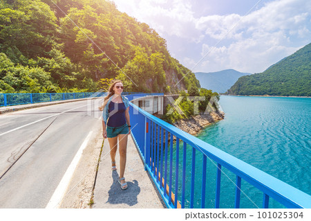 Young woman walking on the bridge across Piva lake in Montenegro Young woman walking on the bridge across Piva lake in Montenegro 101025304