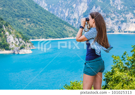 Young woman using binoculars exploring the nature at the Piva lake in Montenegro Young woman using binoculars exploring the nature at the Piva lake in Montenegro 101025313