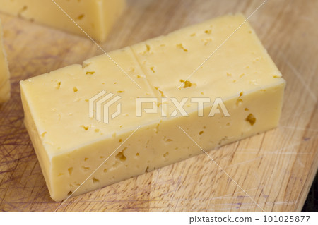 Hard cheese with holes cut into thick pieces on a cutting board Hard cheese with holes cut into thick pieces on a cutting board 101025877