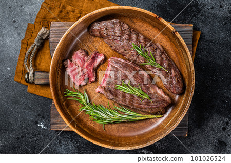Fried sirloin flap or flank beef steak with herbs in a wooden plate. Black background. Top view 101026524