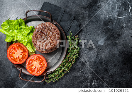 Tasty grilled burger beef patty with tomato, spices and lettuce in kitchen tray. Black background. Top view. Copy space 101026531