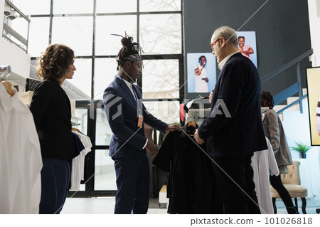 Elderly customer wanting to buy formal suit, asking showroom employee for help to choose the right clothes. Senior man buying fashionable merchandise and stylish accessories in clothing store Elderly customer wanting to buy formal suit, asking showroom employee for help to choose the right clothes. Senior man buying fashionable merchandise and stylish accessories in clothing store 101026818