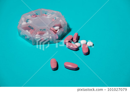 Organizer weekly shots on blue background with Copy space for your text. Closeup of medical pill box with doses of tablets for daily take medicine with white pink drugs and capsules. Daily vitamins at 101027079