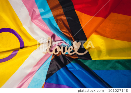 Wooden word love with heart romance on Rainbow LGBTQIA flag made from silk material. Valentine's Day greeting card. Symbol of LGBTQ pride month. Equal rights. Peace and freedom. Support LGBTQIA 101027148