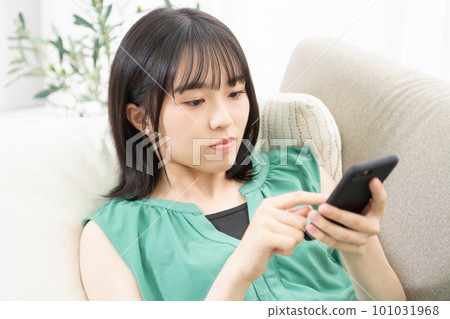 Young woman lying on her back on the sofa and using a smartphone Young woman lying on her back on the sofa and using a smartphone 101031968