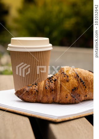 Fresh baked chocolate croissant on paper cup with lid for tea to go. Empty paper notebook. Freelancer's place of work. Study and work. Remote business education. Making plans for next week year. Being 101032642