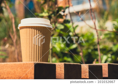 Eco recycling paper cup with coffee or tea on kraft paper on wooden table. Breakfast on the street in the park on bench. Take away coffee to go. Copy space for text. Disposable Cardboard 101032667