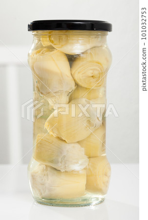 Glass jar with preserved marinated artichokes on table, nobody 101032753