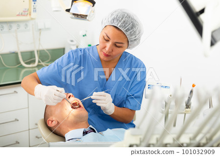 Focused woman dentist treats a man patient Focused woman dentist treats a man patient 101032909
