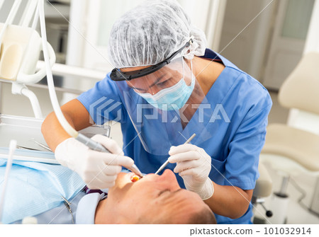 Female dentist drilling tooth to male patient Female dentist drilling tooth to male patient 101032914