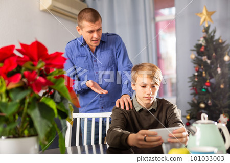 Boy with phone playing game, father trying to speak with him 101033003