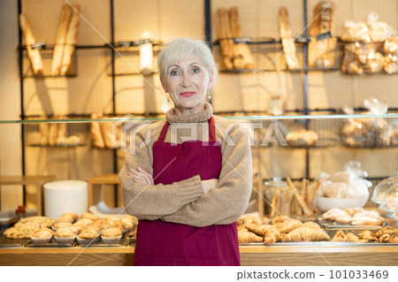 Elderly bakery saleswoman in maroon apron posing with arms crossed 101033469