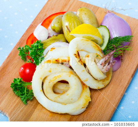 Tasty squid rings at plate with potatoes and fresh vegetables and herbs Tasty squid rings at plate with potatoes and fresh vegetables and herbs 101033605