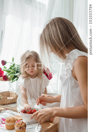 A little blonde girl with her mom on a kitchen countertop decorated with peonies. The concept of the relationship between mother and daughter. Spring atmosphere. A little blonde girl with her mom on a kitchen countertop decorated with peonies. The concept of the relationship between mother and daughter. Spring atmosphere. 101033784