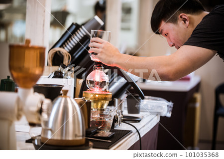 Professional coffee maker - Barista using coffee siphon brewing hot espresso at coffee shop coffee brewing syphon alternative method. Startup Business Concept. Professional coffee maker - Barista using coffee siphon brewing hot espresso at coffee shop coffee brewing syphon alternative method. Startup Business Concept. 101035368