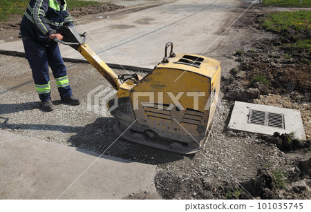 Worker use vibratory plate compactor at road construction site 101035745