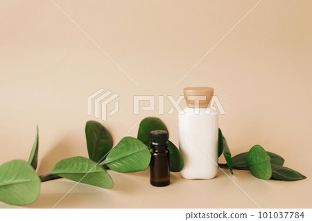 Cosmetic set of two bottles for layout packaging of cream and oil for skin care on a beige background with green leaves. The concept of an organic product of natural beauty. Cosmetic set of two bottles for layout packaging of cream and oil for skin care on a beige background with green leaves. The concept of an organic product of natural beauty. 101037784