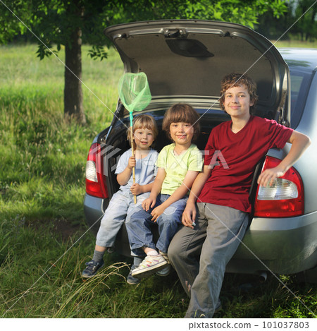 Three cheerful child sitting in the trunk of a car on nature Three cheerful child sitting in the trunk of a car on nature 101037803