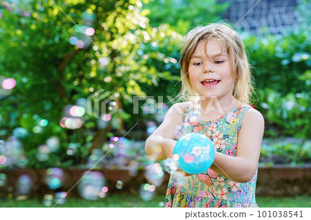 Happy little blonde preschool girl having fun with blowing soap bubble blower. Cute child playing on sunny summer day. Happy active funny healthy kid. Activity for children. Happy little blonde preschool girl having fun with blowing soap bubble blower. Cute child playing on sunny summer day. Happy active funny healthy kid. Activity for children. 101038541