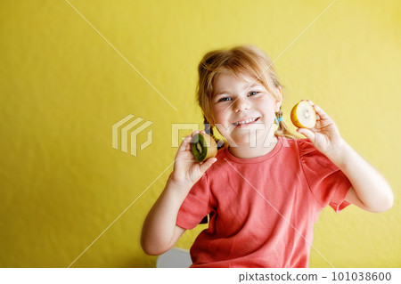 Happy little child girl with yellow and green kiwi fruits on yellow background. Preschool girl smiling. Healthy fruits for children Happy little child girl with yellow and green kiwi fruits on yellow background. Preschool girl smiling. Healthy fruits for children 101038600