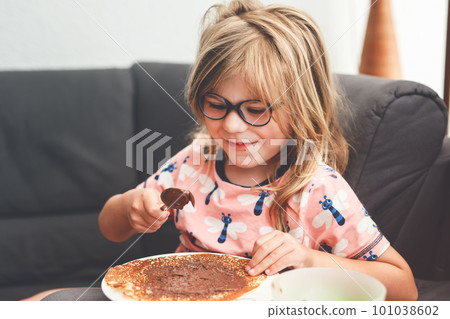 Adorable little girl having breakfast, eating pancakes with chocolate cream. Preschool child smiling. Sweet food for children. Adorable little girl having breakfast, eating pancakes with chocolate cream. Preschool child smiling. Sweet food for children. 101038602