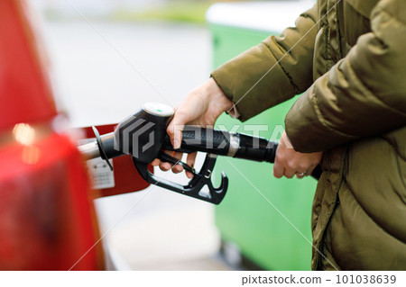 Close-up of hands of woman at self-service gas station, hold fuel nozzle and refuel the car with petrol, diesel, gas. Close up of filling auto with gasoline or benzine. Self service gas pump 101038639