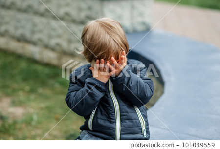 Upset child covering his face at home. Kid hiding behind palms of his hands. 101039559
