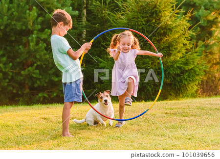 Children playing with pet dog jumping through hula hoop 101039656