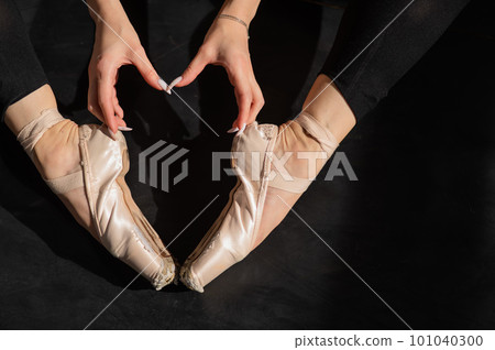 A faceless ballerina sits on the floor and makes a heart shape with her hands and pointe shoes. Top view. A faceless ballerina sits on the floor and makes a heart shape with her hands and pointe shoes. Top view. 101040300