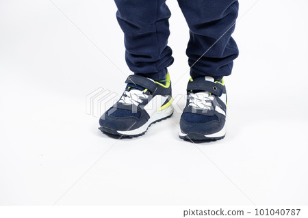 Childrens shoes. Blue kids running shoes sneakers on the legs of a five- or six-year-old boy on a white background. Childrens shoes. Blue kids running shoes sneakers on the legs of a five- or six-year-old boy on a white background. 101040787