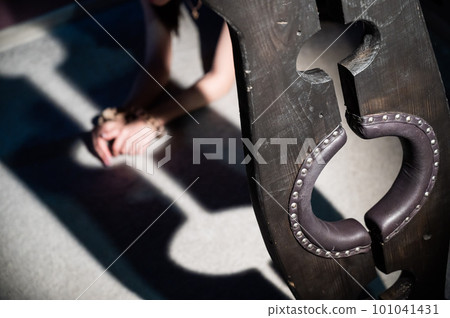 Female hands in wooden shackles during role-playing games. Shameful pillar and leather cuffs for sex. BDSM Domination and punishment. 101041431