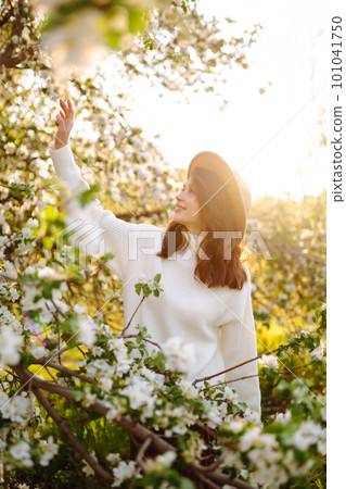 Smiling woman with hat posing in blooming spring park. The concept of relax, travel. Fashion style. 101041750