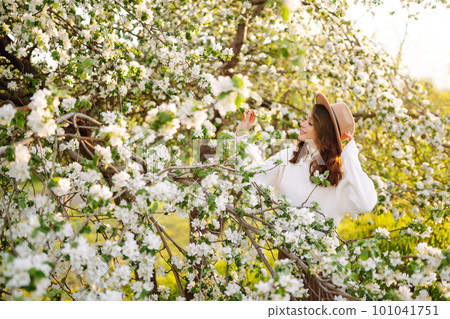 Smiling woman with hat posing in blooming spring park. The concept of relax, travel. Fashion style. 101041751