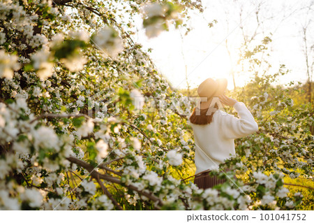 Smiling woman with hat posing in blooming spring park. The concept of relax, travel. Fashion style. 101041752