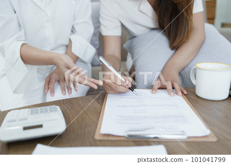 Portrait of young Asian female agent offering life insurance to client using document, calculator and tablet in product presentation. Portrait of young Asian female agent offering life insurance to client using document, calculator and tablet in product presentation. 101041799