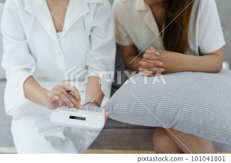Portrait of young Asian female agent offering life insurance to client using document, calculator and tablet in product presentation. 101041801