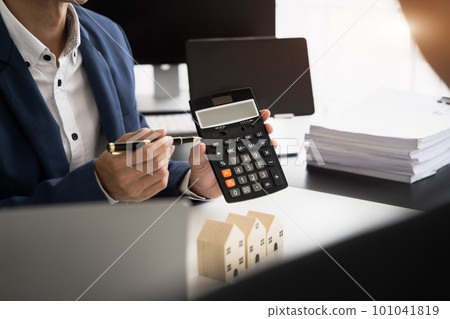 home loan officer uses a calculator with a house plan on a wooden table. home loan officer uses a calculator with a house plan on a wooden table. 101041819
