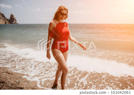 Young woman in red bikini on Beach. Blonde in sunglasses on pebble beach enjoying sun. Happy lady in one piece red swimsuit relaxing and sunbathing by turquoise sea ocean on hot summer day. Close up Young woman in red bikini on Beach. Blonde in sunglasses on pebble beach enjoying sun. Happy lady in one piece red swimsuit relaxing and sunbathing by turquoise sea ocean on hot summer day. Close up 101042061