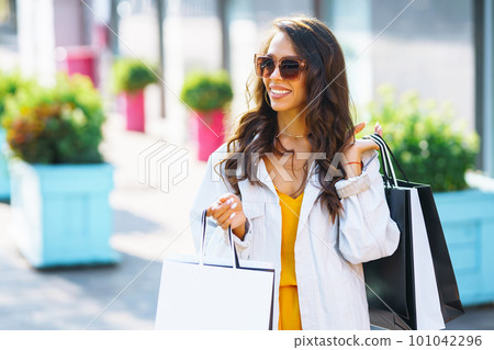 Fashion woman with shopping bags walking on street. Spring Style. Consumerism, shopping, lifestyle. Fashion woman with shopping bags walking on street. Spring Style. Consumerism, shopping, lifestyle. 101042296
