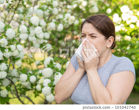 Caucasian woman suffers from allergies and sneezes while walking in the park. 101042740