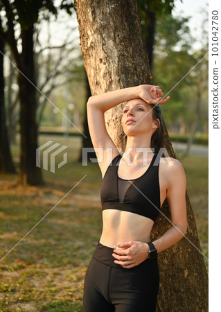 Tired sporty woman leaning on tree trunk, resting after running in the park. Healthy lifestyle concept Tired sporty woman leaning on tree trunk, resting after running in the park. Healthy lifestyle concept 101042780