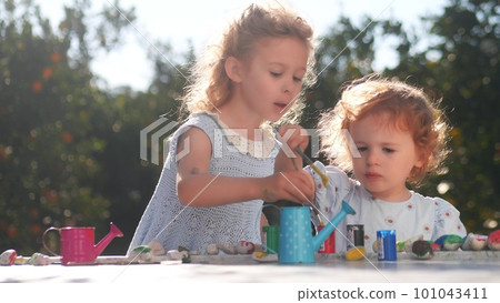 Two little sisters paint on stones in the garden together Two little sisters paint on stones in the garden together 101043411